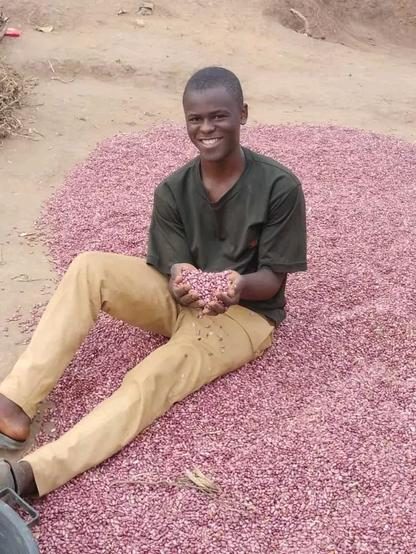 Joshua Kevins sitting among beans drying in the sun, holding a handful