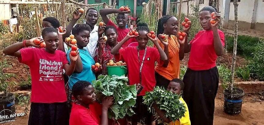 Youth members of Nutritious Foods Uganda holding freshly harvested tomatoes and greens